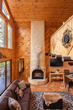 A cozy interior with a fireplace, wooden walls, a sofa, and a dining area.