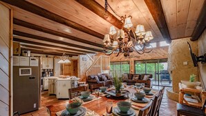 A spacious dining area with a wooden table set for a meal, surrounded by comfortable seating. A kitchen with modern appliances is visible in the background. - Free Dollywood Tix/Views/Pool/Spacious/Arcade (Sevierville)