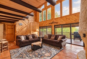 A spacious living area with a wooden interior, a staircase, and large windows offering views of the outdoors.