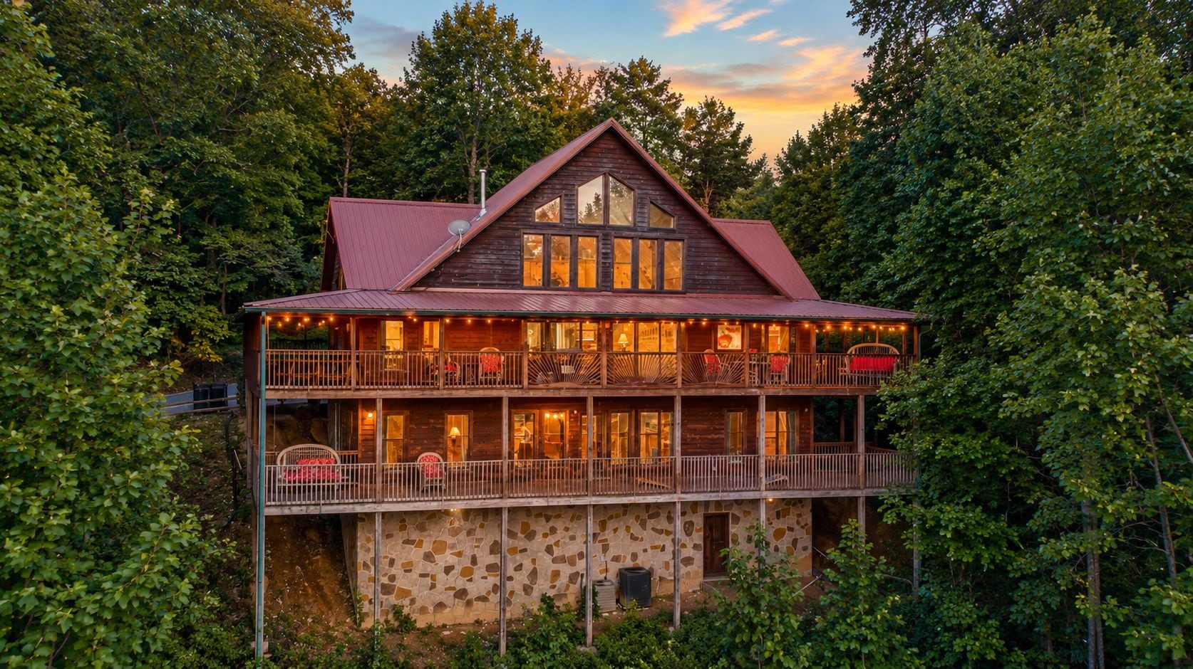 A two-story wooden cabin with a stone foundation, multiple balconies, and a large window on the upper level.