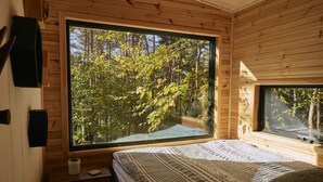 Ein Schlafzimmer mit großem Fenster und Blick auf einen Wald.