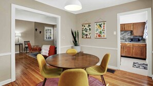 Un comedor con una mesa redonda y cuatro sillas, una lámpara colgante y una cocina visible a través de un vano abierto.