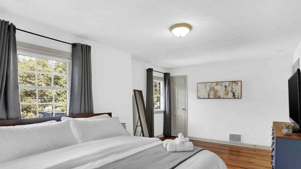 Habitación de hotel con una cama grande, televisión de pantalla plana, un cuadro en la pared y una ventana con cortinas.