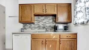 Una cocina con armarios de madera, lavavajillas, microondas y salpicadero de azulejos.