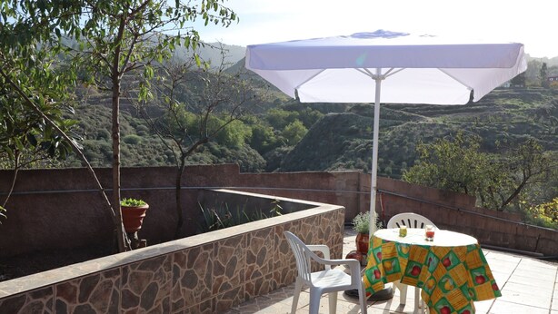 An outdoor patio with a table, chairs, a white umbrella, and potted plants. - Casa Rural en San Mateo, con Finca Propia (CN)