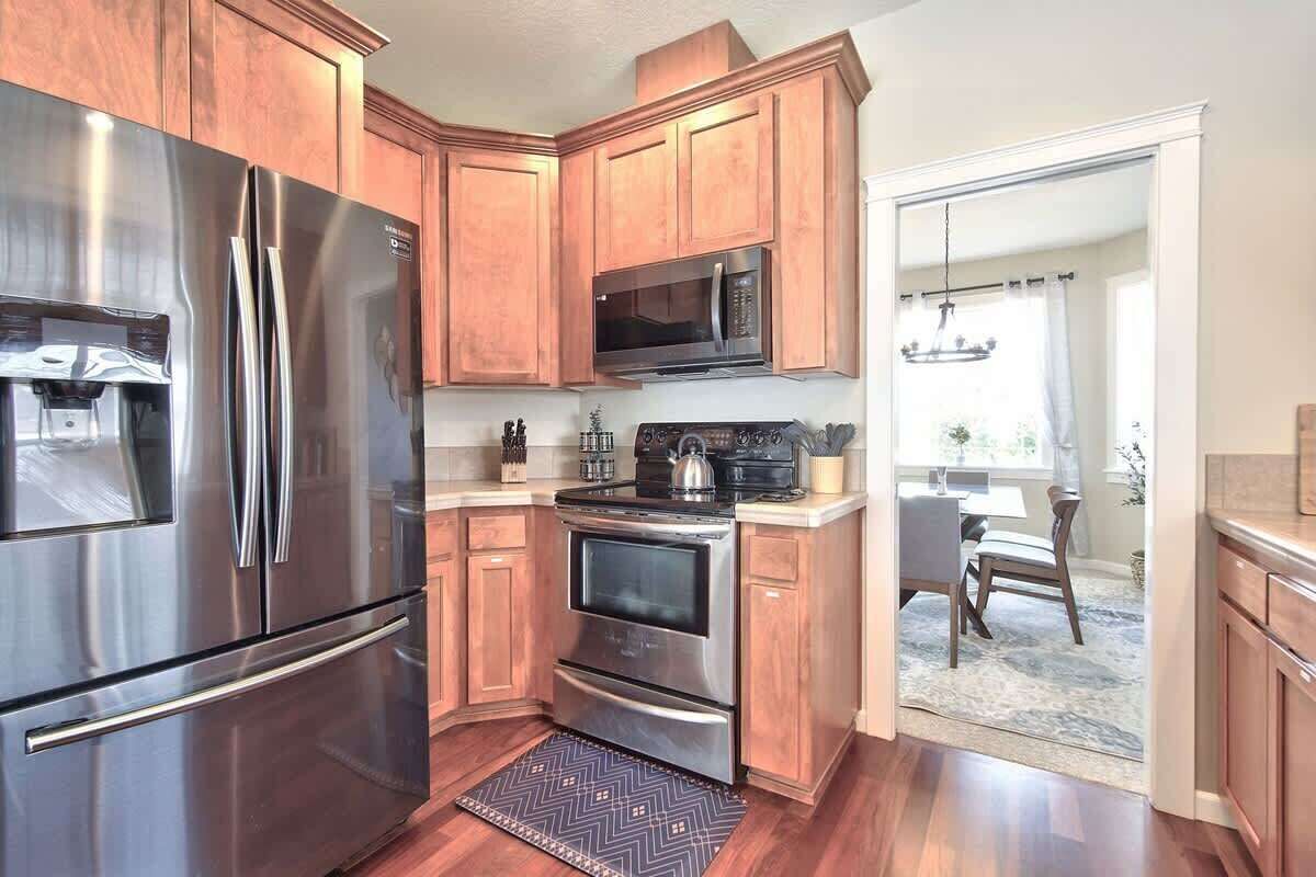 A modern kitchen with stainless steel appliances, wooden cabinets, and a dining area visible through an open doorway.