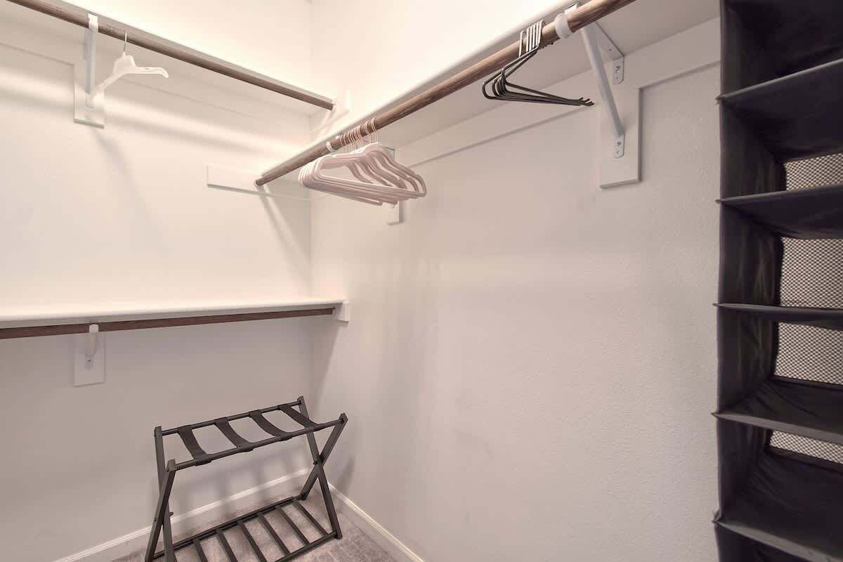 A walk-in closet with metal shelves, a metal drying rack, and a wooden rod with a white hanger.