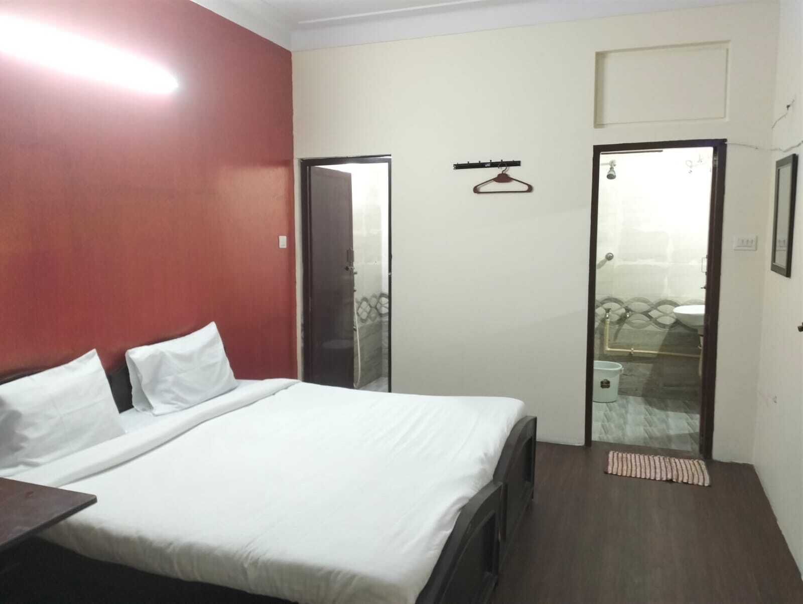 Habitación de hotel con cama, una mesita, perchero y baño visible a través de una puerta abierta.
