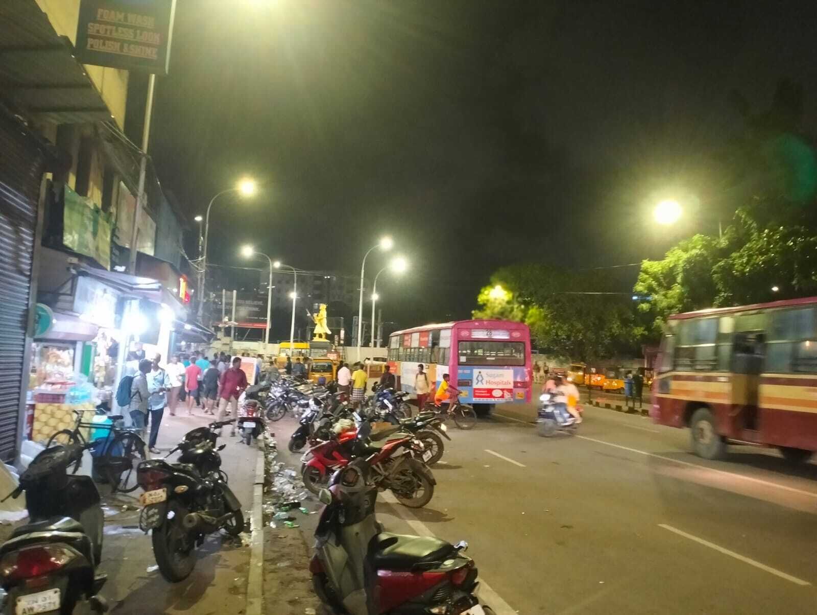 A street scene at night with parked motorcycles, a bus, and pedestrians.