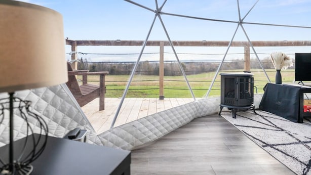 A cozy room with a large window, a comfortable sofa, a table, and a wood-burning stove. - Skye's Dome - A relaxing getaway (Debert)