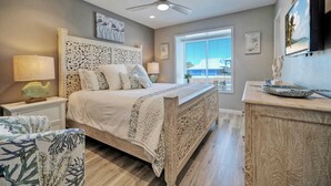 A bedroom with a bed, nightstands, a ceiling fan, a window with a view, and a TV mounted on the wall.