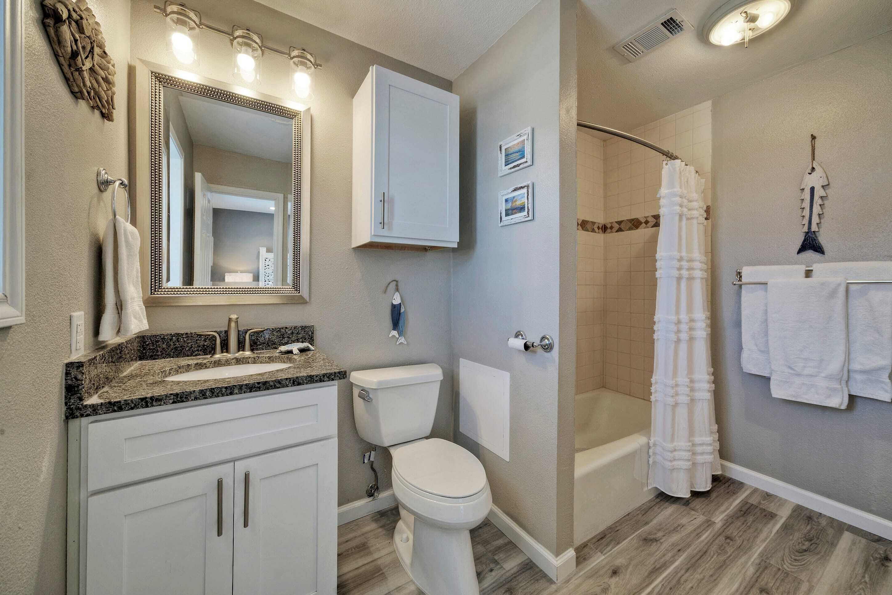 A bathroom with a sink, toilet, and shower. There are towels hanging on the wall and a mirror above the sink.