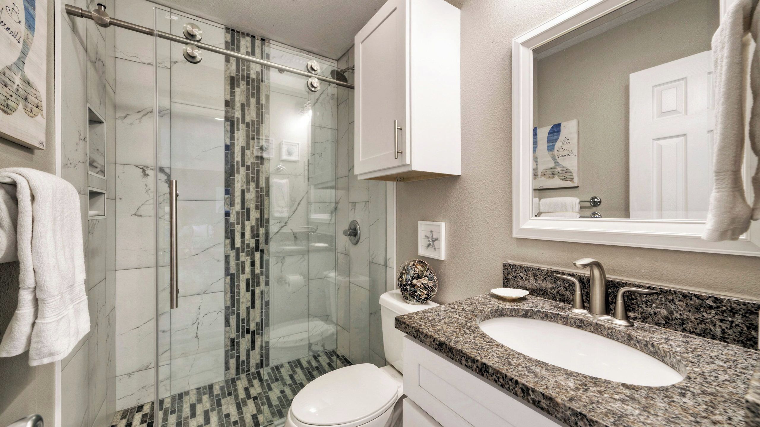 Un baño moderno con ducha acristalada, inodoro blanco e inodoro con encimera de granito.