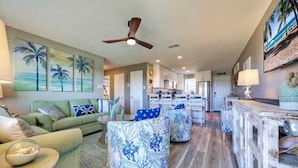 A spacious living room with a green sofa, round ottomans, and a dining area with a white table. - 2BR Condo w/ Gulf Views, 2 Pools, Courts Blue Water Bliss by Avantstay (Port Aransas)