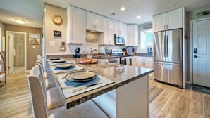 A modern kitchen with a central island, stainless steel appliances, and a 'BEACH HOUSE' sign. - 2BR Condo w/ Gulf Views, 2 Pools, Courts Blue Water Bliss by Avantstay (Port Aransas)