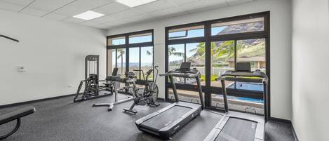 Un gimnasio con equipo de ejercicio, ventanas amplias y vistas a una piscina.