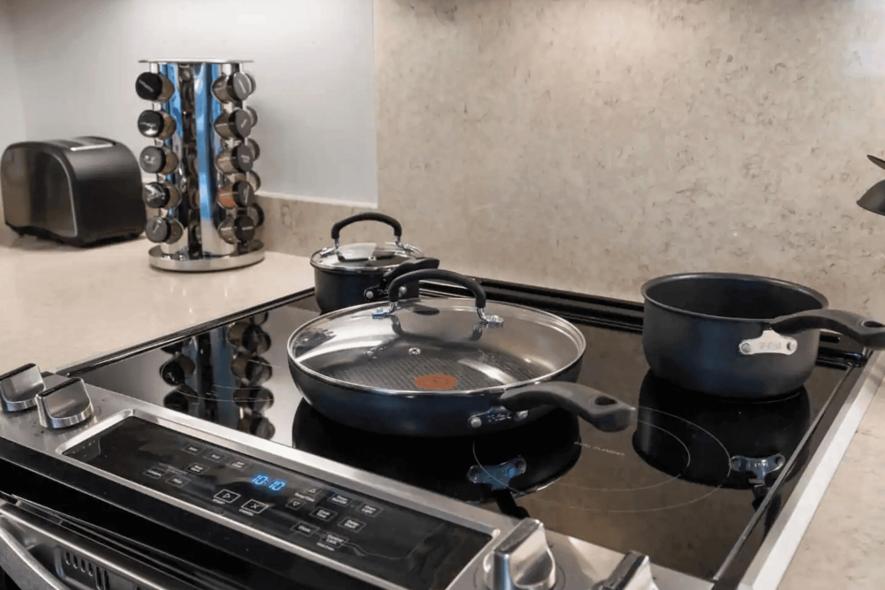 Una cocina moderna con una placa de inducción negra, un hervidor, un tostador y un juego de tazas medidoras.