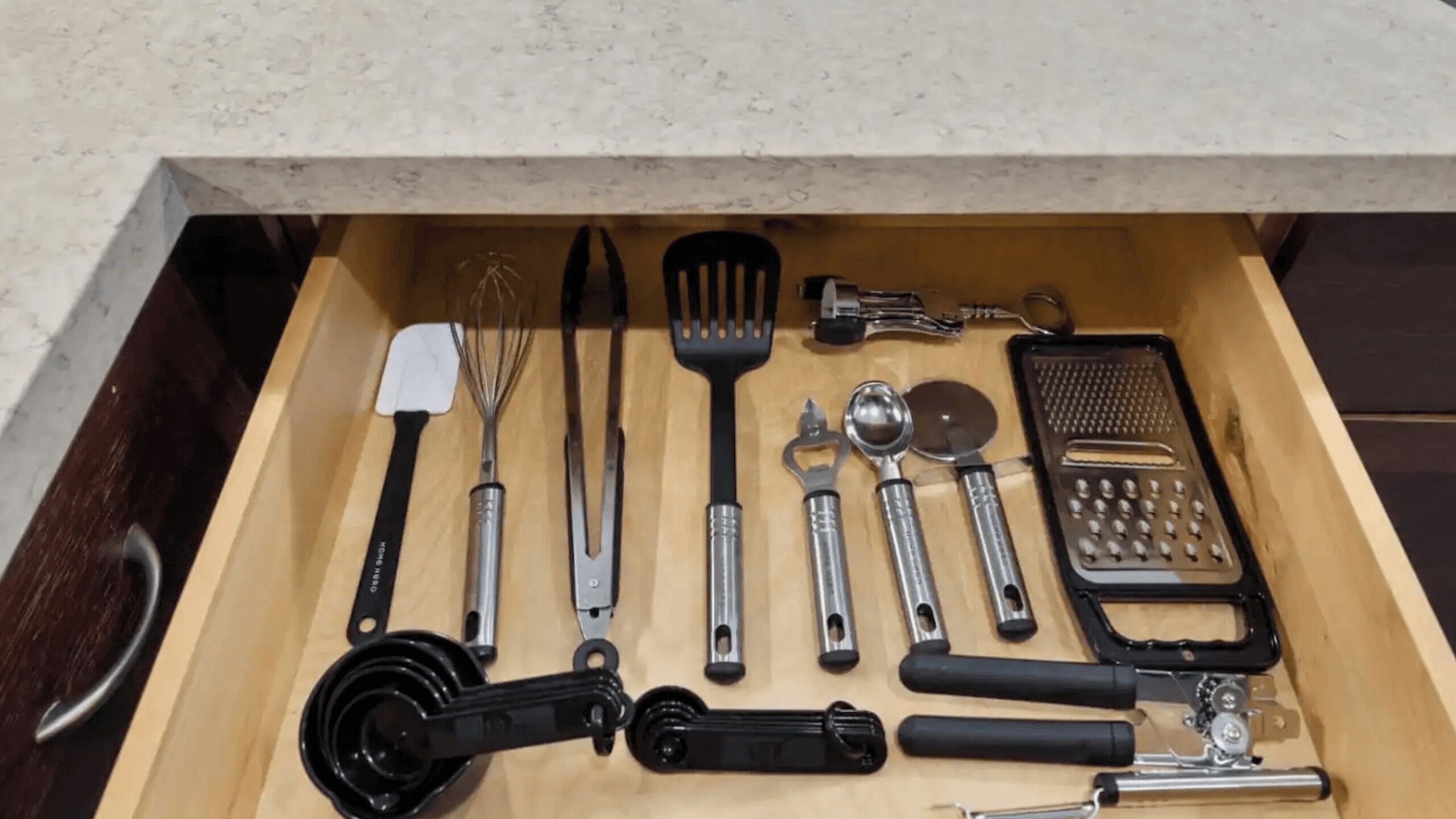 A drawer with various kitchen utensils including a whisk, spatula, and grater.