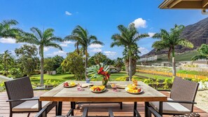 A wooden table with chairs on a deck, surrounded by palm trees and a view of a residential area with houses and a mountain in the background. - Aloha Breeze by Avantstay Ocean View, Near Beach (Waianae)
