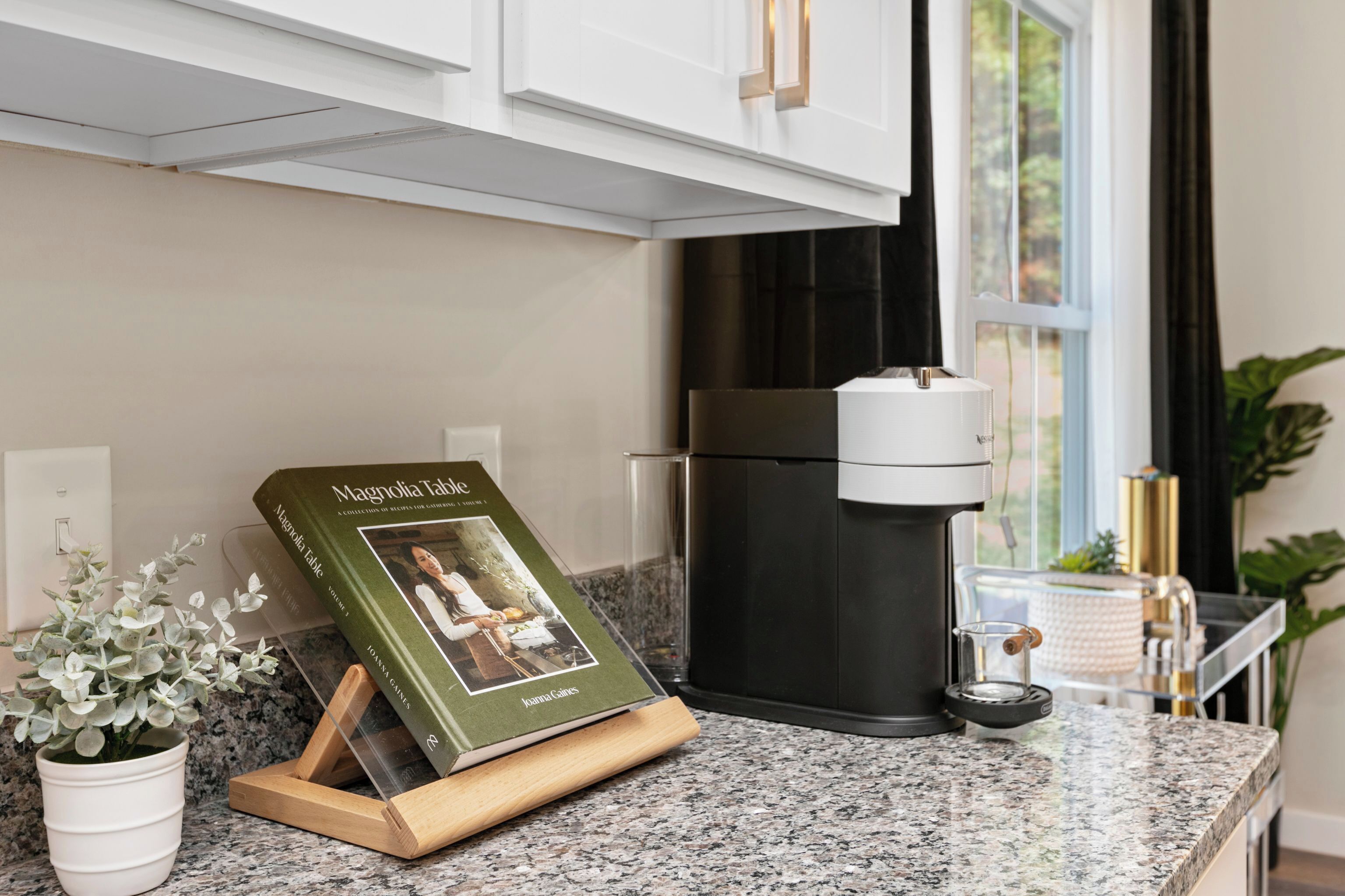 Cuina amb cafetera, un llibre anomenat 'Magnolia Table' i una planta en test.