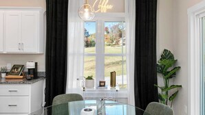 A modern kitchen with a glass table, white cabinets, and a view of the outdoors. - 10 Mins to Downtown Deck w/ Fire Pit Modern Haven Bradford by Avantstay (Asheville)