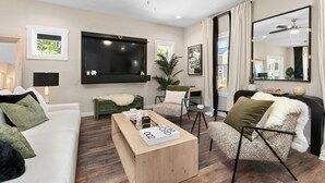 A modern living room with a sofa, armchair, coffee table, TV, and a ceiling fan. - 10 Mins to Downtown Deck w/ Fire Pit Modern Haven Bradford by Avantstay (Asheville)