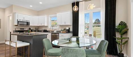 A modern kitchen with white cabinets, a central island, and a glass dining table.