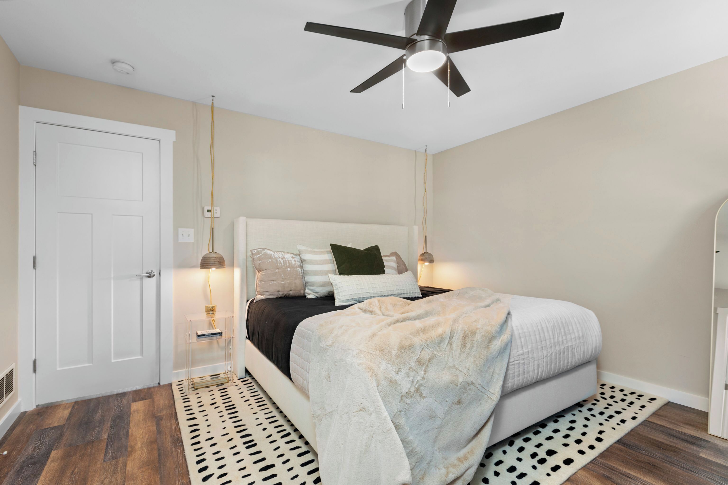 A bedroom with a bed, a ceiling fan, a white door, and a patterned rug.