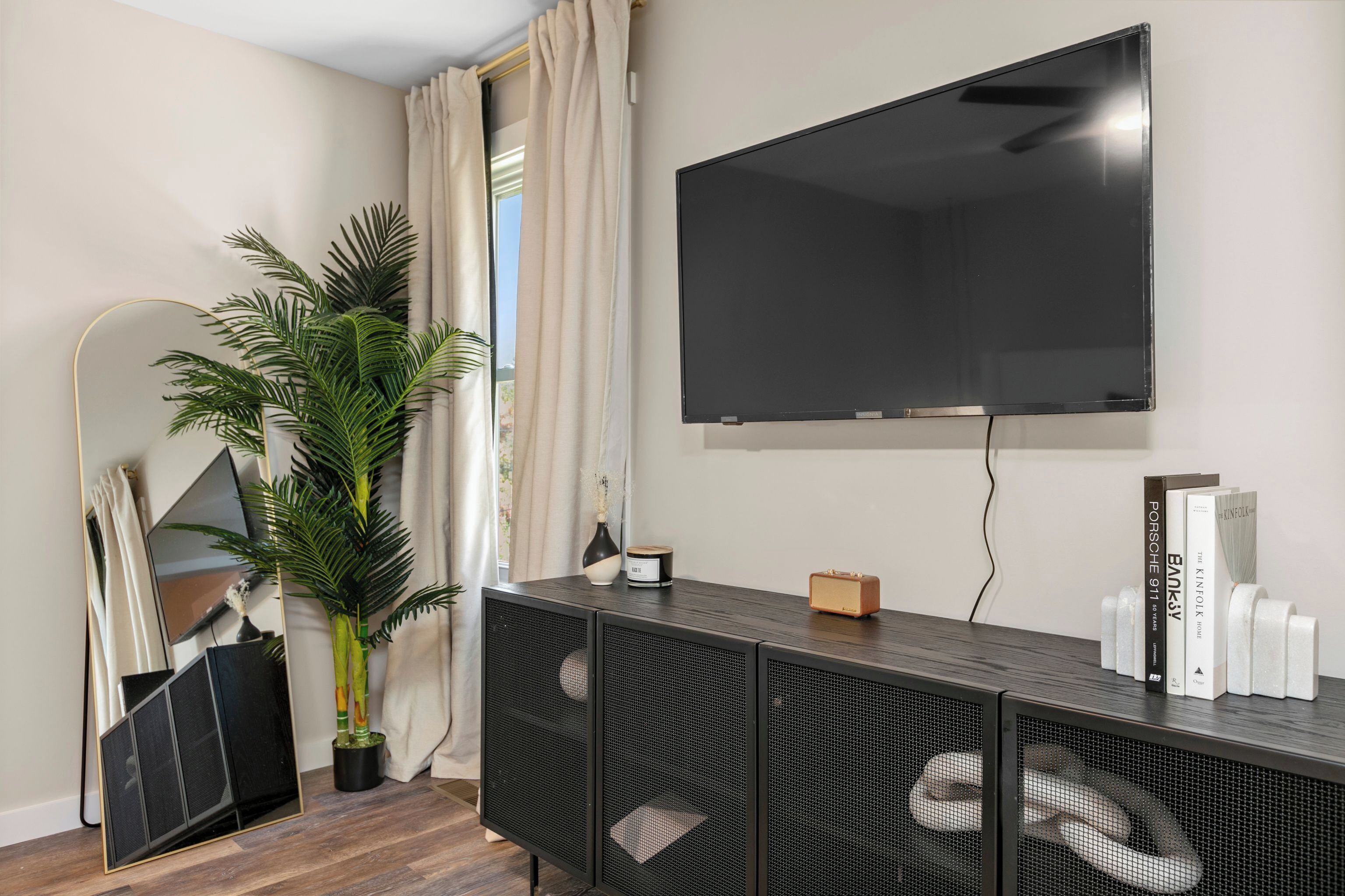 En moderne stue med et stort fladskærms-tv, en stueplante, et spejl og et konsolbord med bøger og pyngeting.
