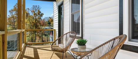 A wooden deck with two wicker chairs and a small table, overlooking a residential area with autumn trees.
