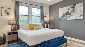 Un dormitorio moderno con una cama grande, mesitas de noche y un banco azul.