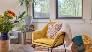 Un salón con un sillón amarillo, una planta en maceta y una alfombra colorida.