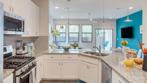 Una cocina moderna con armarios blancos, estufa a gas, microondas y un amplio ventanal.