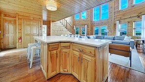 A spacious living area with a large wooden ceiling, a central island with a sink, a staircase, and a sofa set. - Scarlet Lodge by Avantstay Game Room + Views (Sevierville)