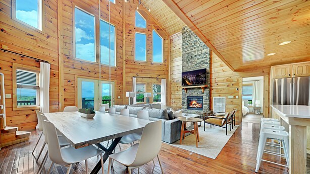 A spacious cabin with a large dining area, a cozy living room, a stone fireplace, and a kitchen with bar stools. - Scarlet Lodge by Avantstay Game Room + Views (Sevierville)