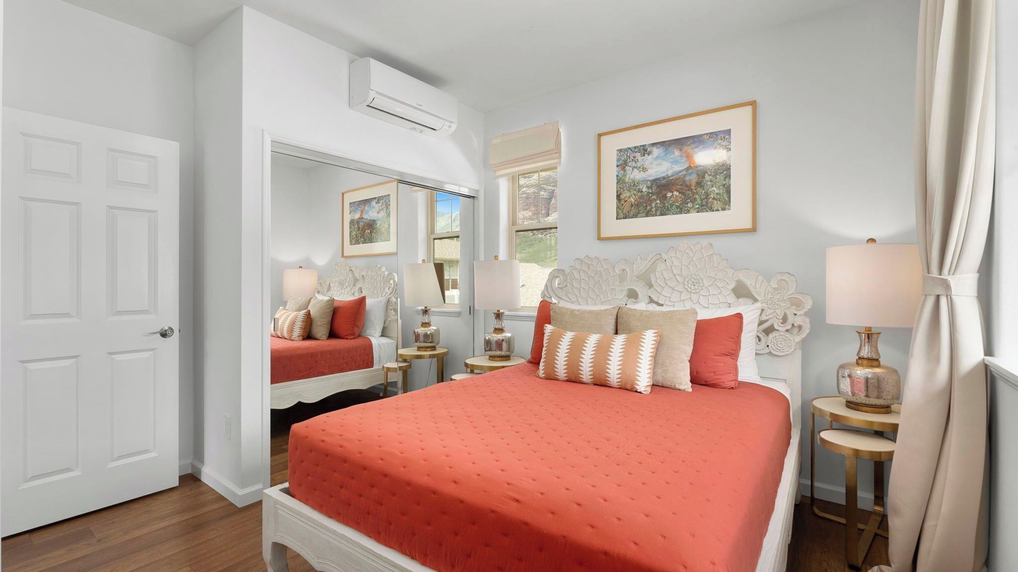 A bedroom with a large bed, two bedside tables, a mirror, and a window with a view.