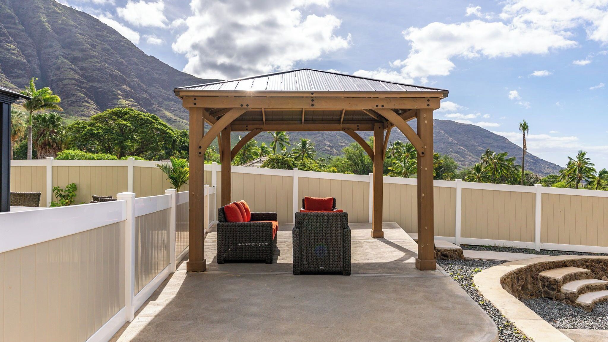A covered outdoor seating area with two wicker chairs and a wooden pergola, overlooking a mountainous landscape.