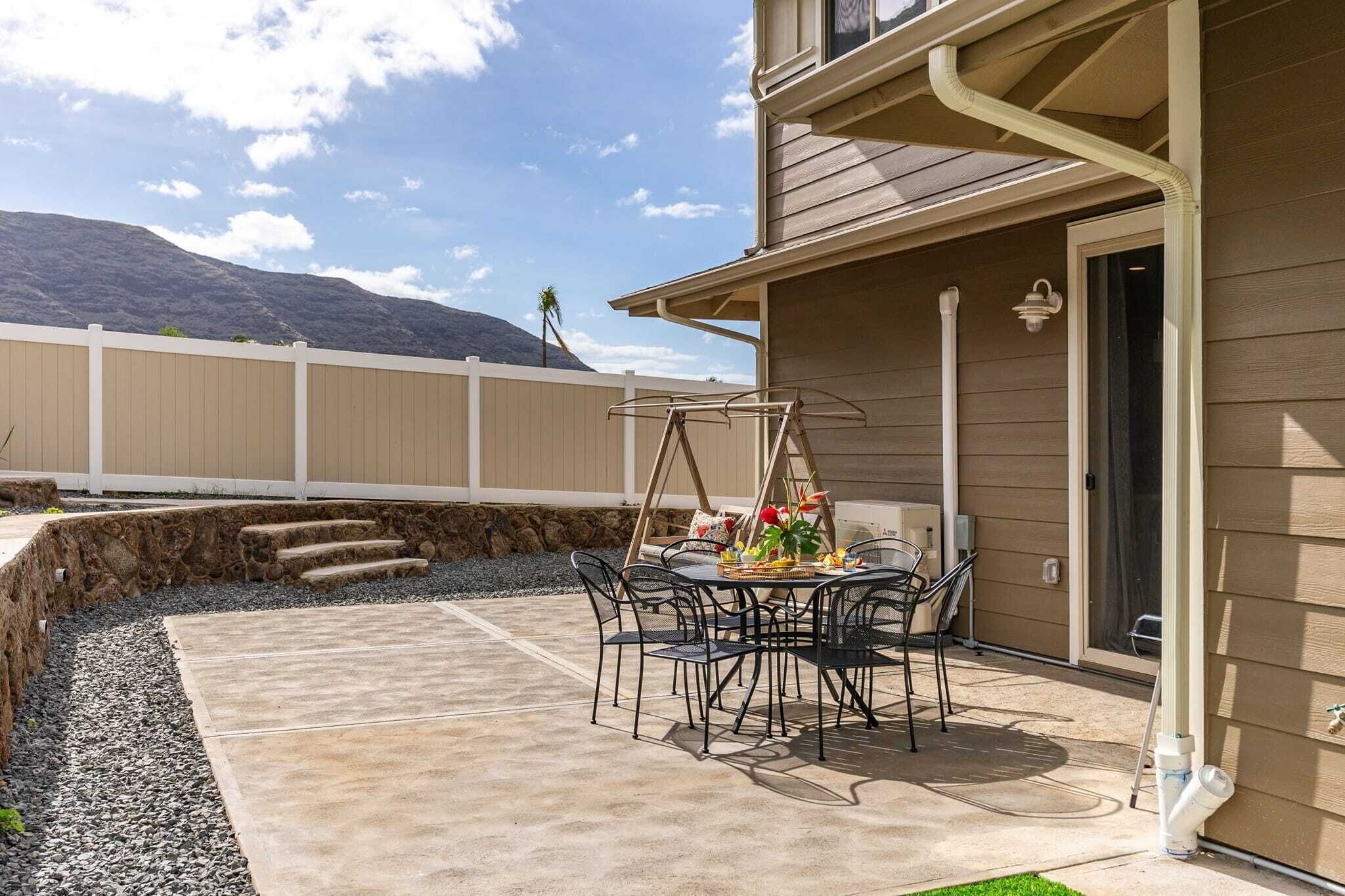 An outdoor patio with a table and chairs, a small garden area, and a view of a mountain.