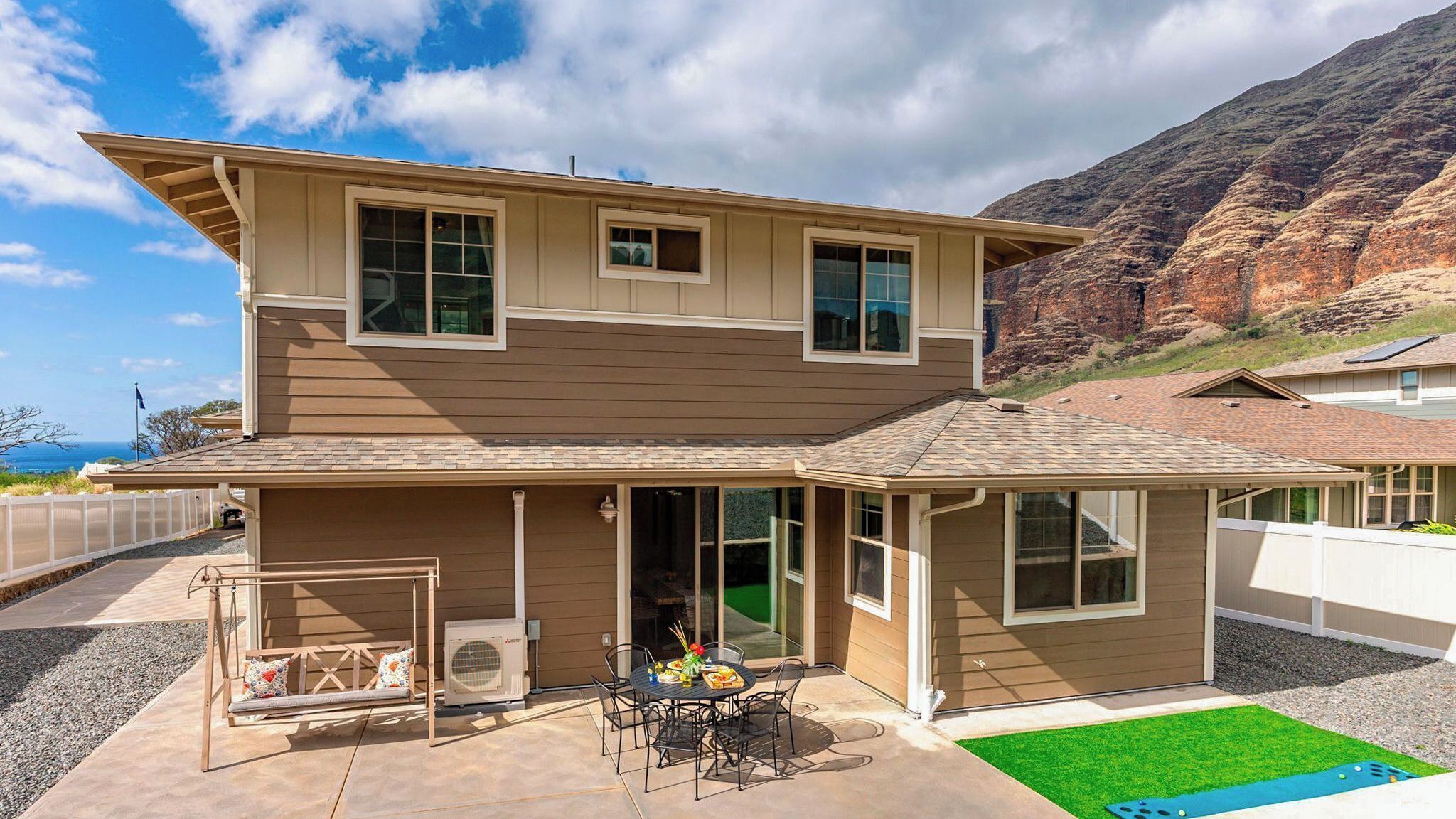 A two-story house with a patio, a swing set, and a view of a mountainous landscape.