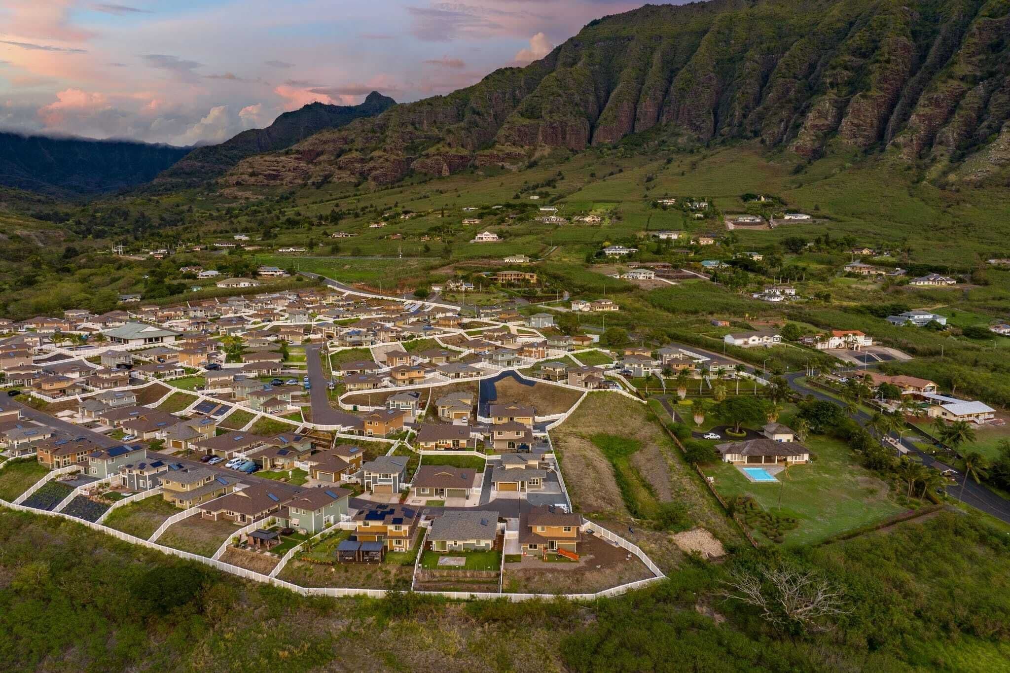 Una zona residencial con casas dispuestas en forma de cuadrícula, rodeada de colinas y montañas verdes.
