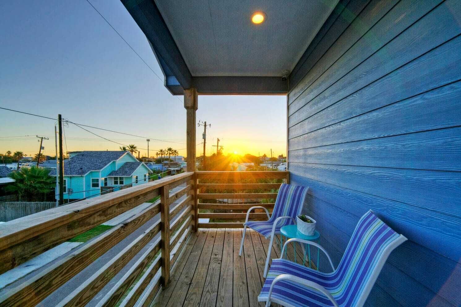 A wooden deck with a railing, two striped chairs, and a small table.