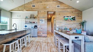 A kitchen with wooden walls, a bar area, and a dining space with stools. - Priv Pool, Walk to Marina + Eateries, 3 Mins to Beach Marlin Azul by Avantstay (Port Aransas)