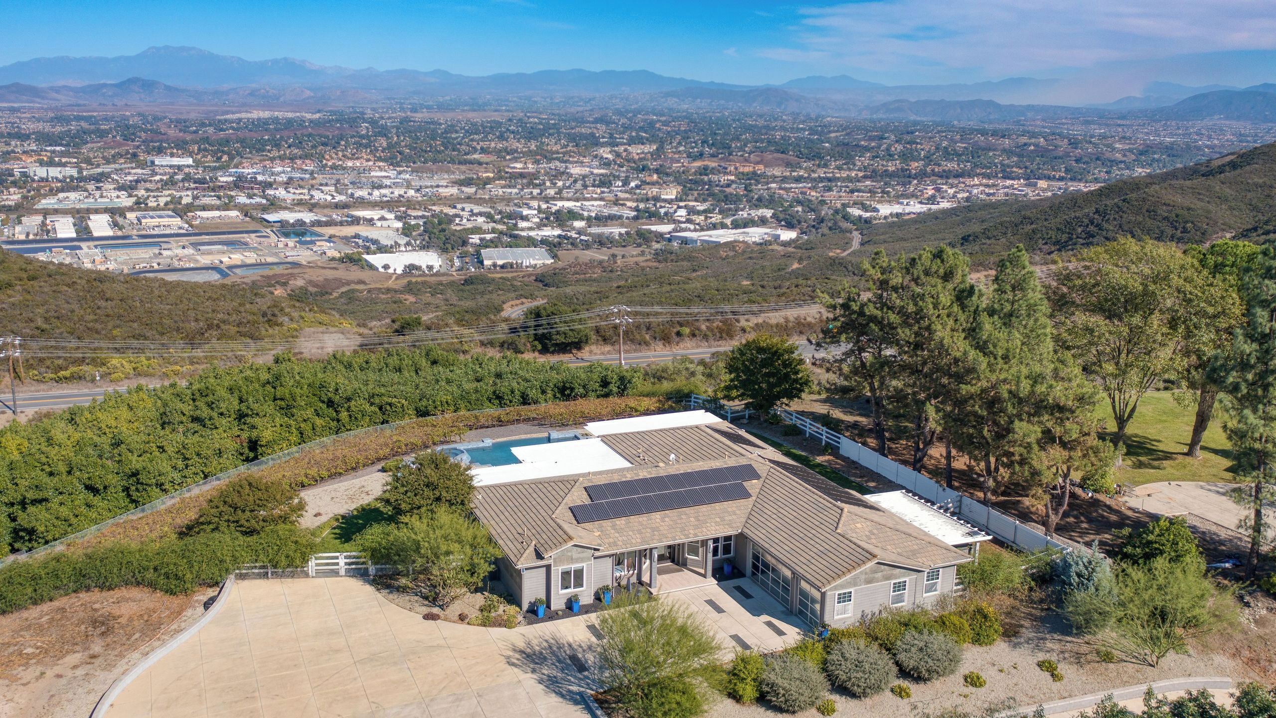 A residential property with a large house, solar panels, and a view of a distant town and mountains.