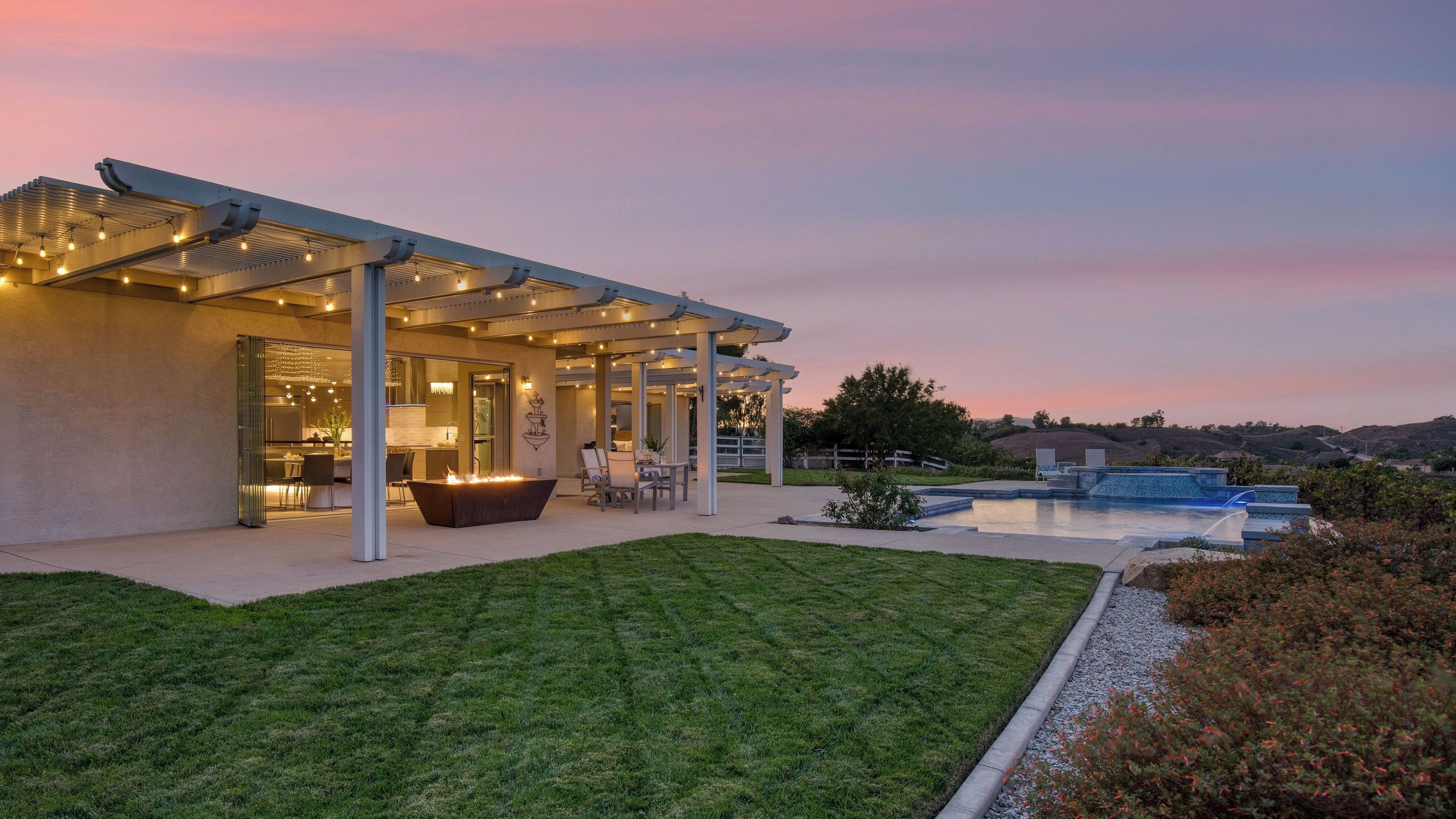 Ein modernes Haus mit überdachter Terrasse, Schwimmbad und gepflegtem Rasen.