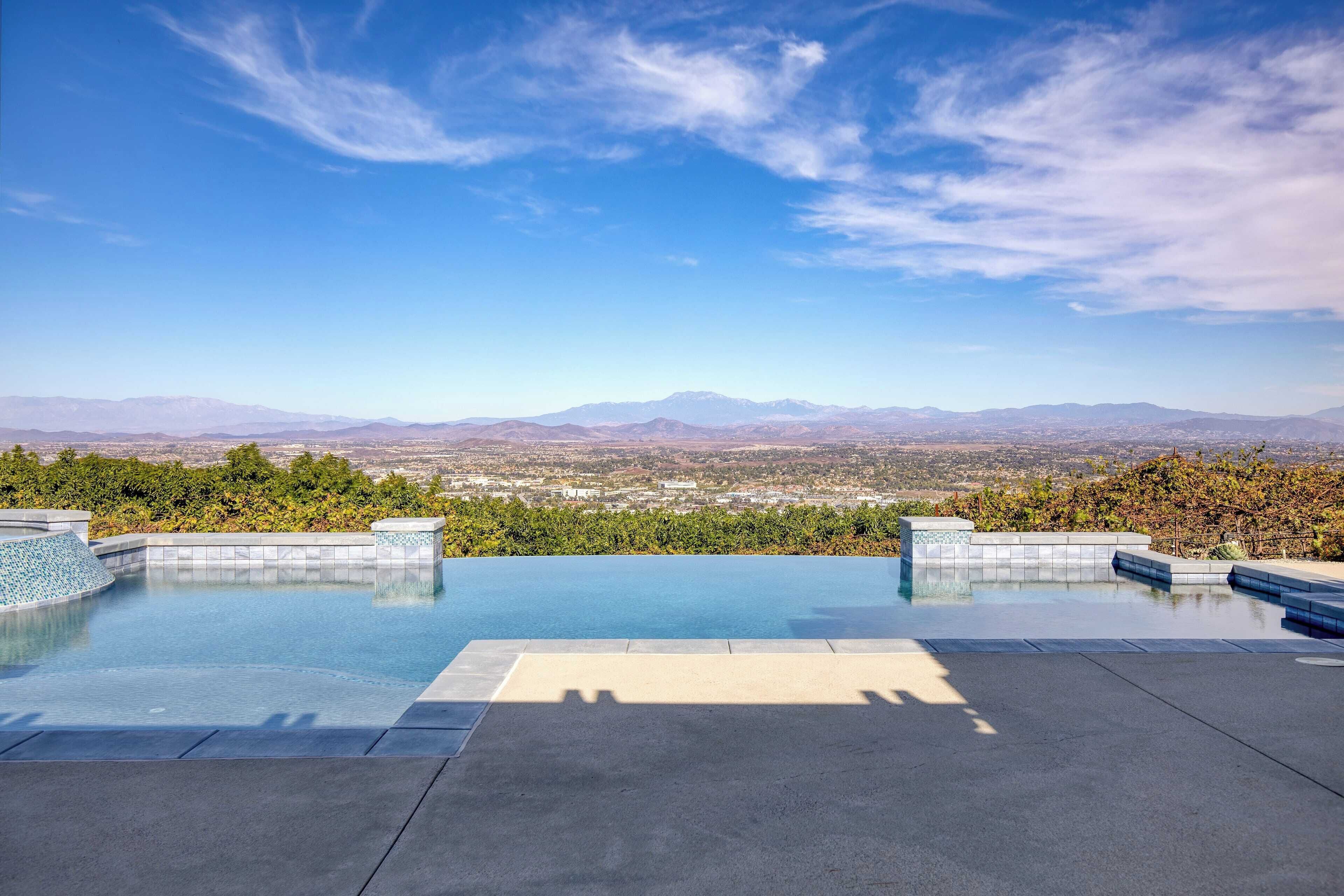 A rooftop infinity pool with a view of distant mountains and a cityscape.