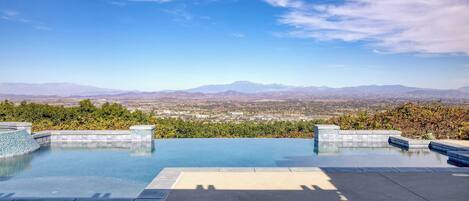 A rooftop infinity pool with a view of distant mountains and a cityscape.