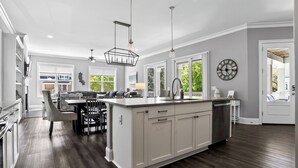 Une cuisine moderne dotée d’un îlot central, de luminaires suspendus et offrant une vue sur l’extérieur.