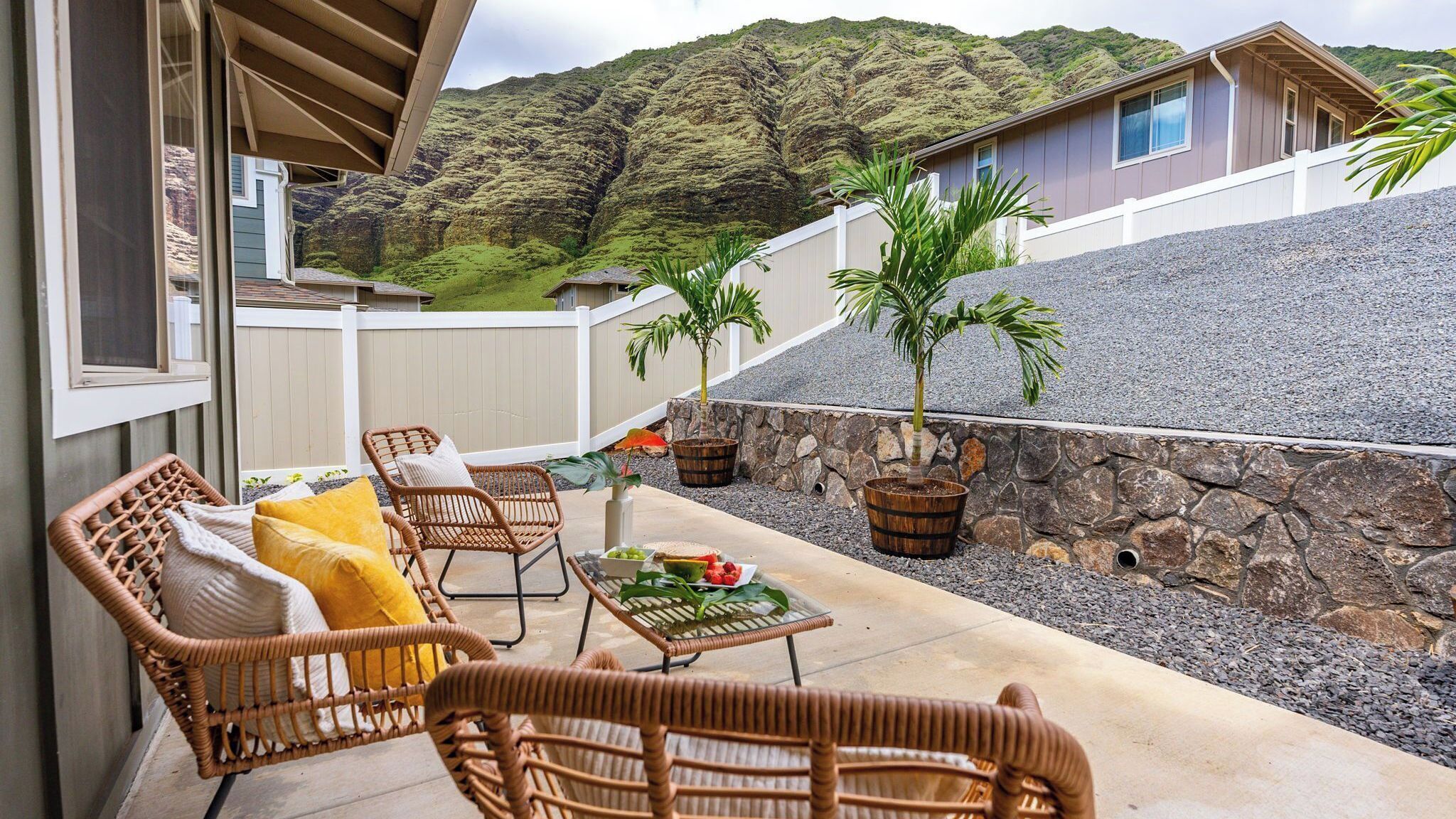 A covered patio with wicker furniture, a table with fruit, and a view of a mountain.