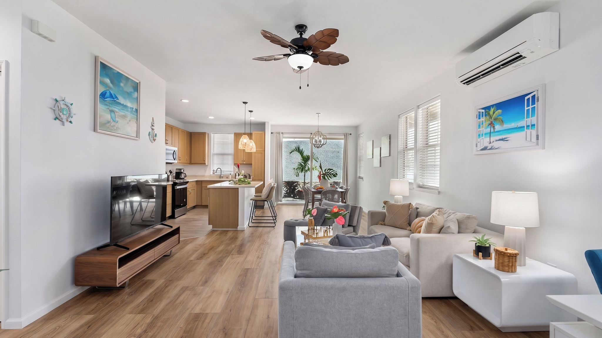 A modern living room with a grey sofa, a dining area with a table and chairs, a kitchen with wooden cabinets, and a ceiling fan.