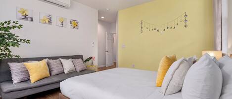 A bedroom with a bed, a grey sofa, and a wall with a string of decorative lights.
